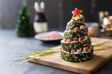 Selbstklebende Fototapeten The concept of sushi on New Year night. Fresh sushi roll with salmon and avocado in a pyramid with Christmas decorations. Traditional japanese food. Sushi in form of christmas tree with copy space. © pijav4uk