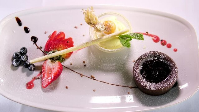 chocolate fondant on white plate with dark chocolate ice cream strawberries drops of syrup beautiful serving in an expensive restaurant. dessert food