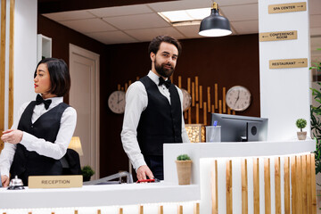 Elegant hotel employee at front desk working on booking enquiries and room reservations with...