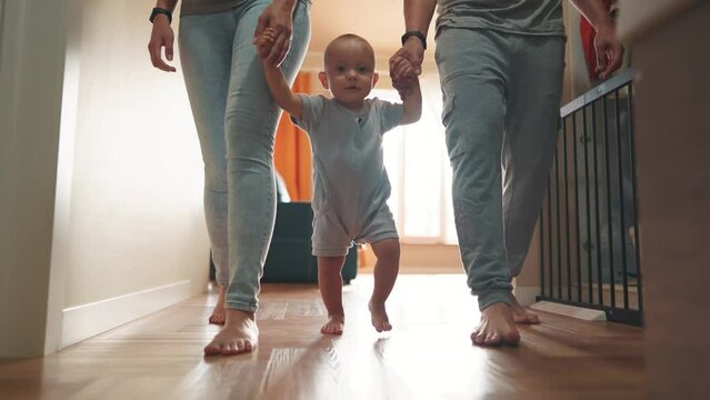 baby with parents first steps. happy family kid dream concept. baby son takes first steps holds family hands silhouette against window indoors. cute baby toddler learning walk with family lifestyle