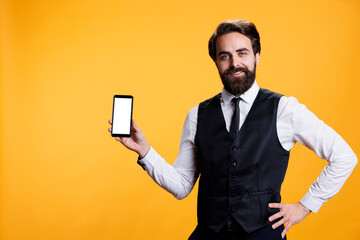 Professional waiter points at white screen on smartphone, presenting isolated copyspace template on...