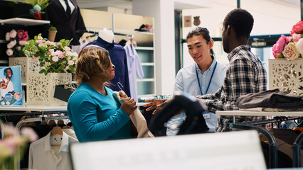 African american customers asking for employee help, explaining clothes fabric during shopping session in modern boutique. Cheeful couple shopping for fashionable merchandise in clothing store