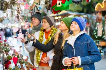 Friendly family with teenage children who came to the Christmas fair in the open air, chooses Christmas souvenirs and toys