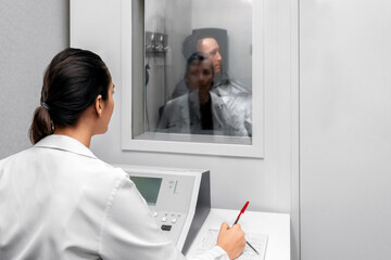 Audiologist woman doing the hearing exam to a mixed race man patient using an audiometer in a...