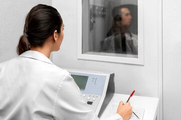 Audiologist woman doing the hearing exam to a mixed race man patient using an audiometer in a...