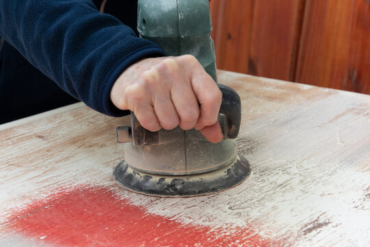 Mano con lijadora quitando pintura vieja de una madera