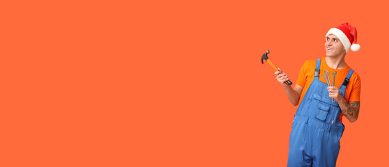 Repairman in Santa hat and with tools on orange background with space for text