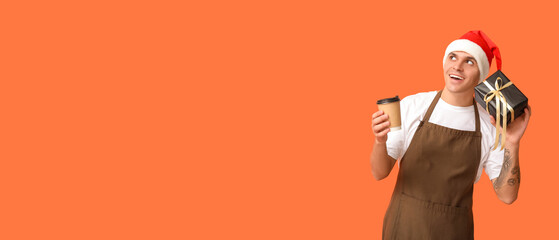 Male barista with Christmas gift and cup of coffee on orange background with space for text