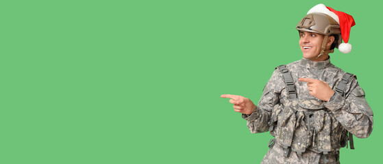 Soldier with Santa hat showing something on green background with space for text