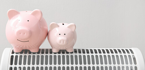 Piggy banks on electric heater against grey background with space for text. Heating saving concept