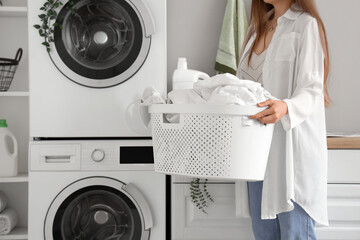 Woman with basket of dirty clothes in laundry room with washing machines