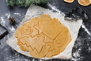 Raw dough and cutters for preparing Christmas cookies on dark background