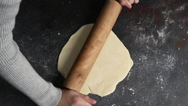 A pastry chef woman rolls out raw yeast dough for buns or pizza.
