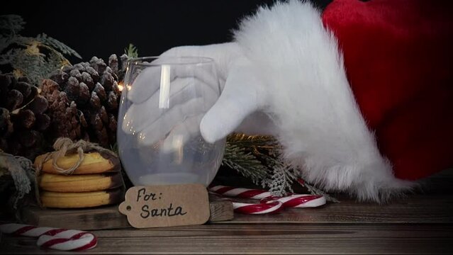 The hand of Santa Claus puts an empty glass of milk on the table.