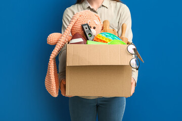 Woman holding box of unwanted stuff for yard sale on blue background