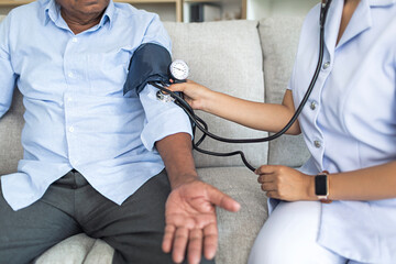Cropped image, Asian female doctor checking old man patient arterial blood pressure at home or...