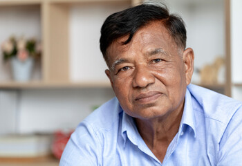 Close-up, old man's face, elderly Asian man thinking and looking at camera sit on couch in living room alone.