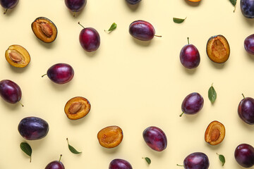 Frame made of fresh ripe plums and leaves on yellow background