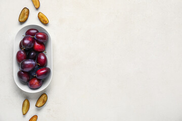 Plate with fresh ripe plums on white background