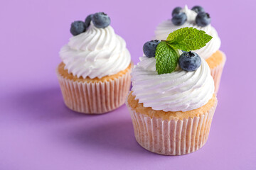 Tasty cupcakes with blueberries on lilac background