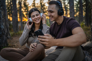 Man and woman young adult couple in nature listen music headphones