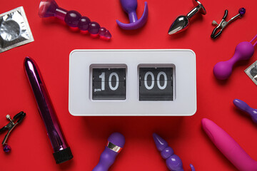 Alarm clock with different toys on red background. Time for sex