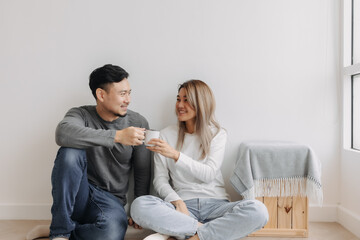Fototapeta na wymiar Happy romantic asian couple lover support with hug and coffee sit on the floor.
