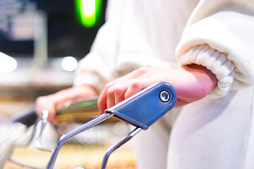 Close-up of a young woman's hand with a grocery cart in a supermarket