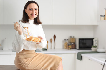 Young woman eating tasty pasta in kitchen