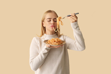 Young woman eating tasty pasta on beige background