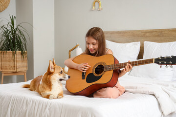 Little girl with cute Corgi dog playing guitar in bedroom