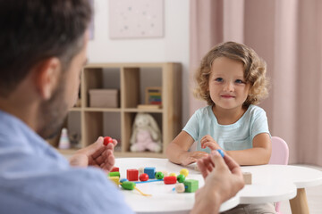 Obraz na płótnie Canvas Motor skills development. Father and daughter playing with wooden lacing toy at table indoors