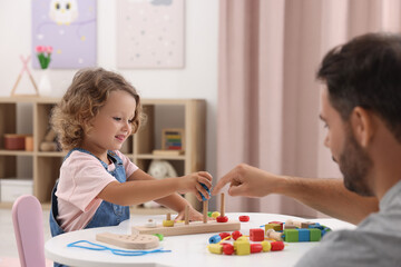 Motor skills development. Father and daughter playing with stacking and counting game at table indoors