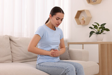 Woman suffering from abdominal pain on sofa at home. Unhealthy stomach