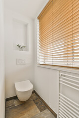 a white bathroom with wooden blinds on the window and toilet in the fore - image was taken from an...