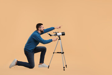 Happy astronomer with telescope pointing at something on beige background. Space for text