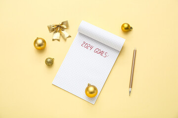 Notebook with text 2024 GOALS, pen and Christmas decor on light yellow background