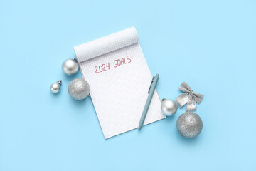 Notebook with text 2024 GOALS, pen and silver Christmas balls on blue background