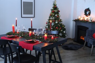 Elegant Christmas table setting with dishware and burning candles in festively decorated room