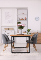 Table, chairs and vase with peonies in stylish dining room