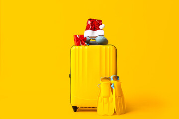 Suitcase with flippers, Santa hat and Christmas gift on yellow background