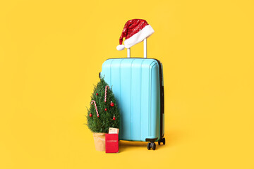 Suitcase with Santa hat, Christmas tree and passport on yellow background