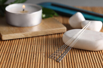 Acupuncture needles, spa stones and burning candle on bamboo mat. Space for text