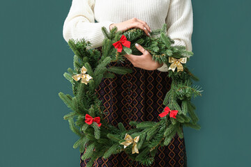 Woman holding beautiful wreath made of fir tree branches on green background