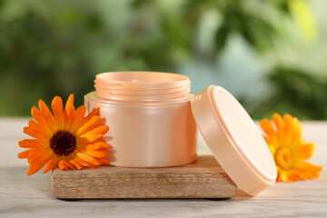 Jar of cream and beautiful calendula flowers on white wooden table outdoors, closeup