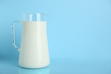 Jug of fresh milk on light blue background, space for text