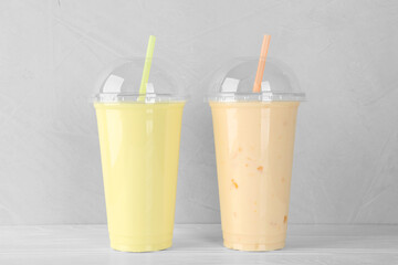 Plastic cups of different tasty smoothie on white wooden table