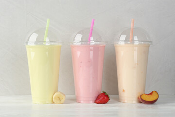Plastic cups of different tasty smoothie and fresh fruits on white wooden table