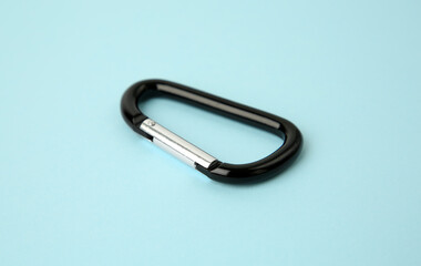 One black carabiner on light blue background, closeup