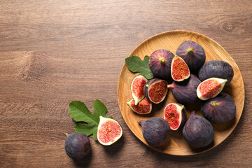 Fototapeta premium Whole and cut ripe figs with leaves on wooden table, flat lay. Space for text